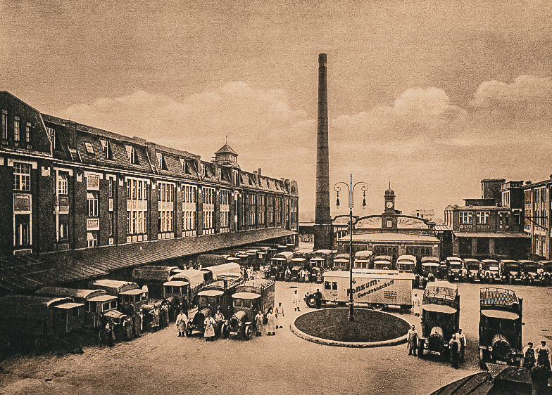 Ein Bild von 1913 wo der Vorplatz des früheren Bäckereikombinats zu sehen ist. Es stehen viele Lieferwägen vor Ort .